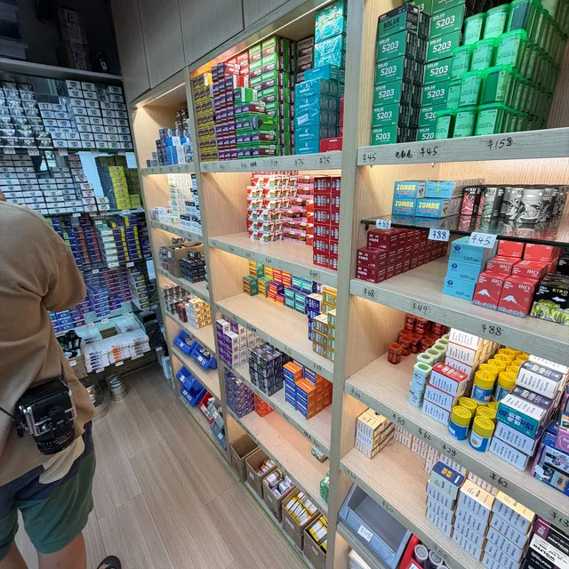 Shelves of respooled motion picture film in small Chinese-brand boxes, a customer with a medium format camera on his hip in the corner of the frame