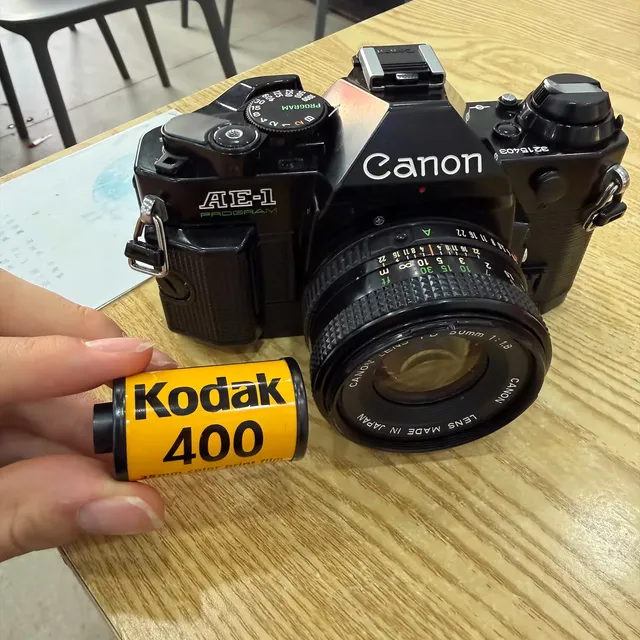 A Canon AE-1 Program on a table with a roll of Kodak UltraMax 400 held in front of it
