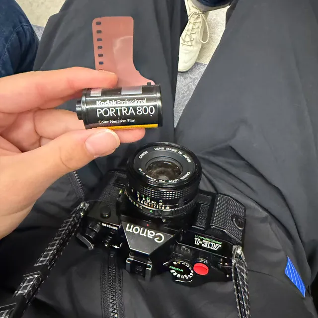 A canister of Kodak Portra 800 held above a Canon AE-1 Program resting on a lap
