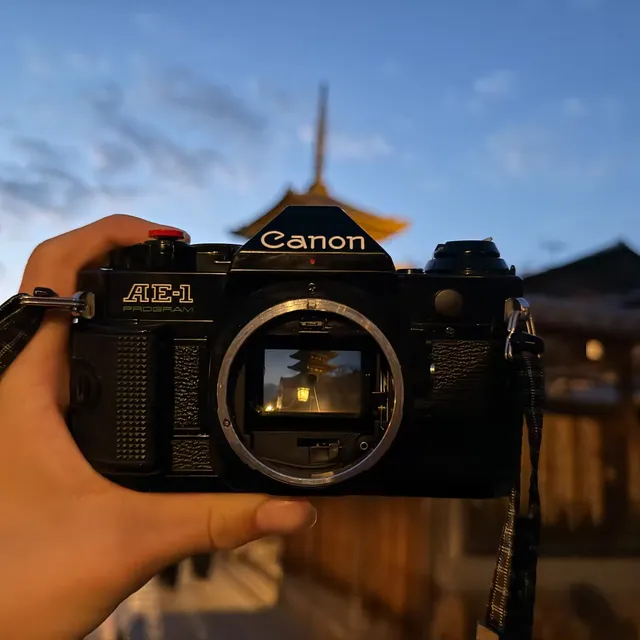 A Canon AE-1 Program with the lens removed, held up so the open mount frames a pagoda in Kyoto